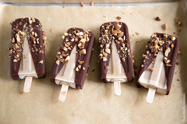 Banana Coconut Ice Pops with dipped in chocolate and almonds in a row on parchment paper.