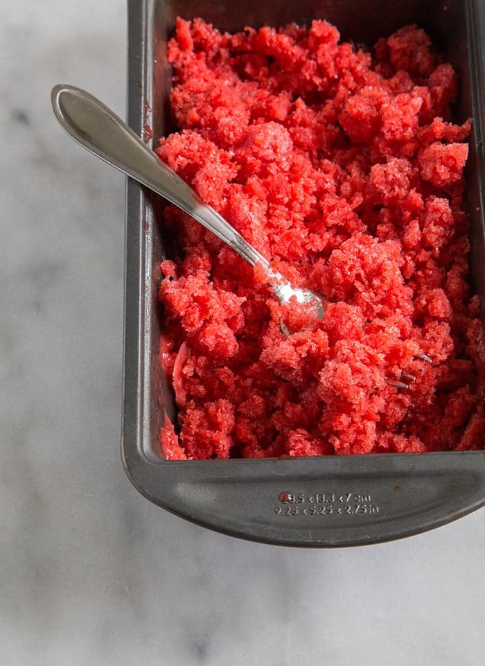close up of freshly scraped strawberry basil granita in a freezer safe loaf pan. 