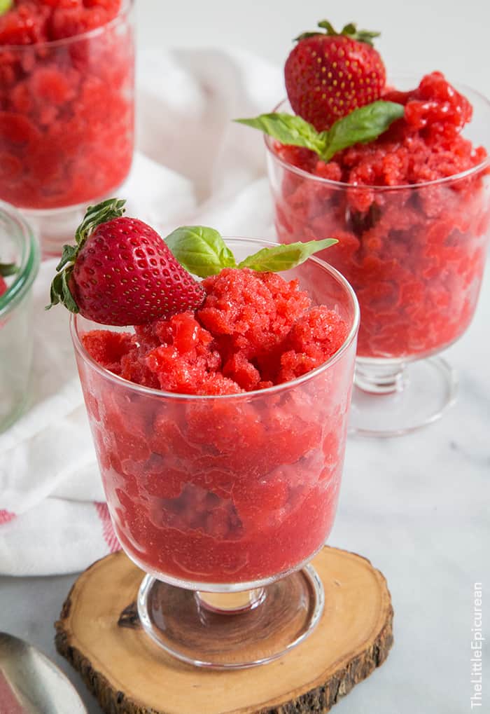 close up of strawberry basil granita in serving cup garnished with fresh strawberry and fresh basil sprig. 