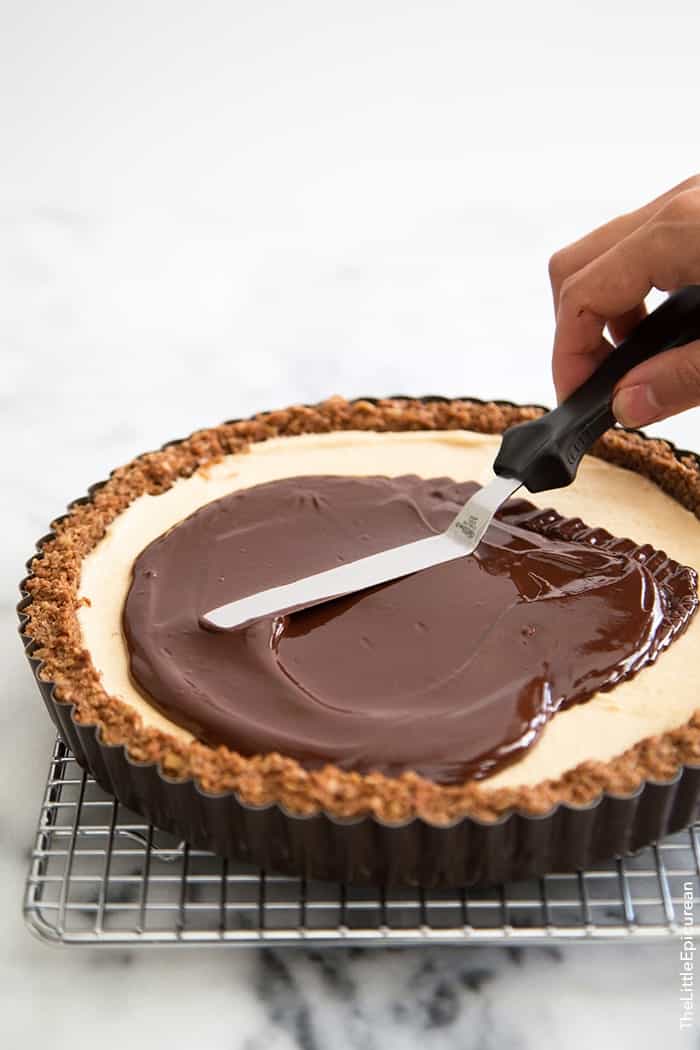 melted chocolate spread atop peanut butter oat tart using mini spatula. 