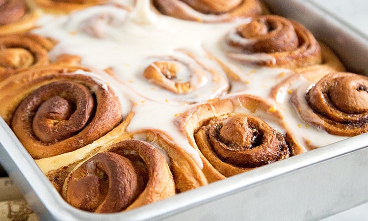 glaze being poured on fresh baked cinnamon rolls.