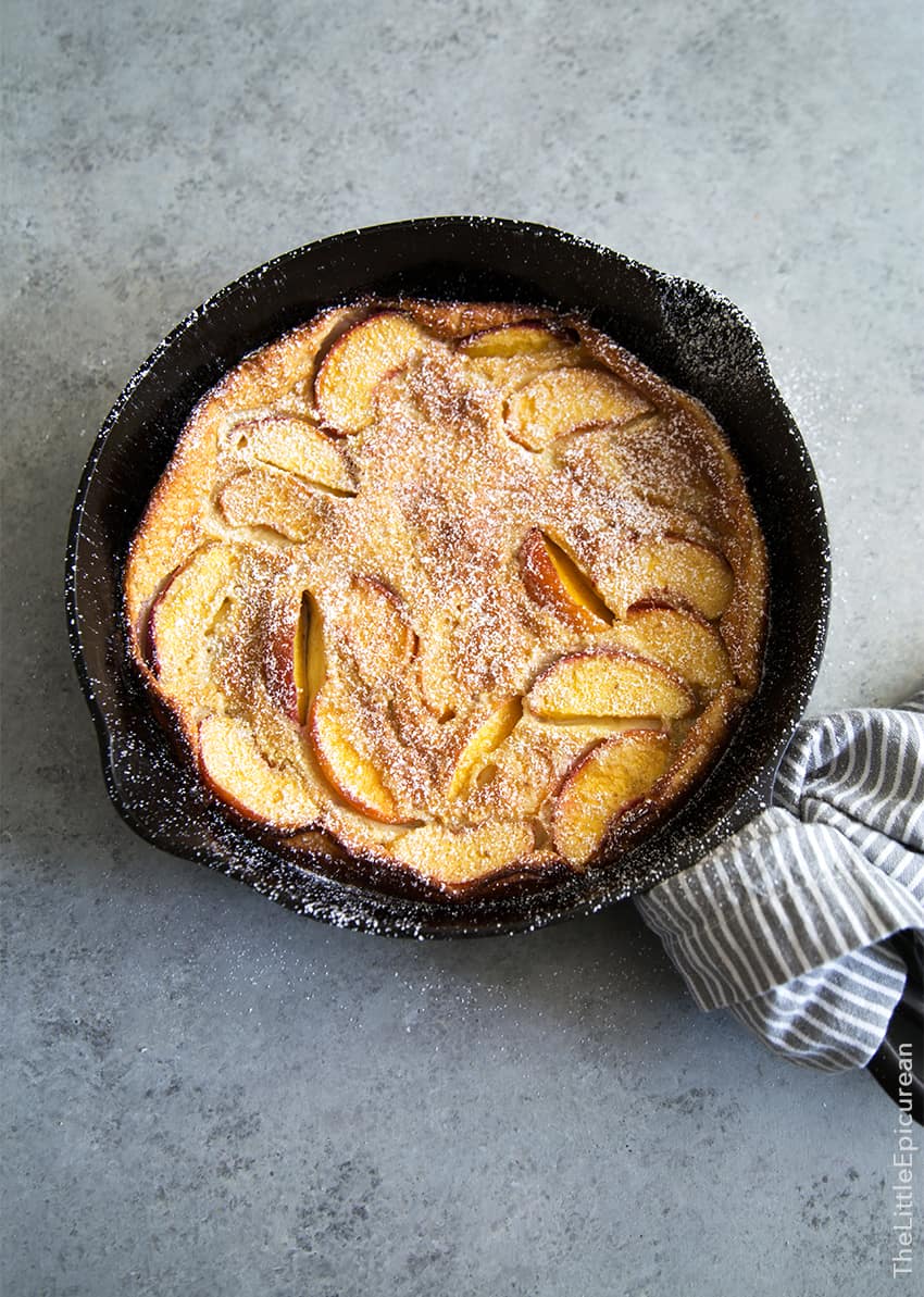 Whiskey Peach Clafoutis dusted with powered sugar in cast iron skillet.