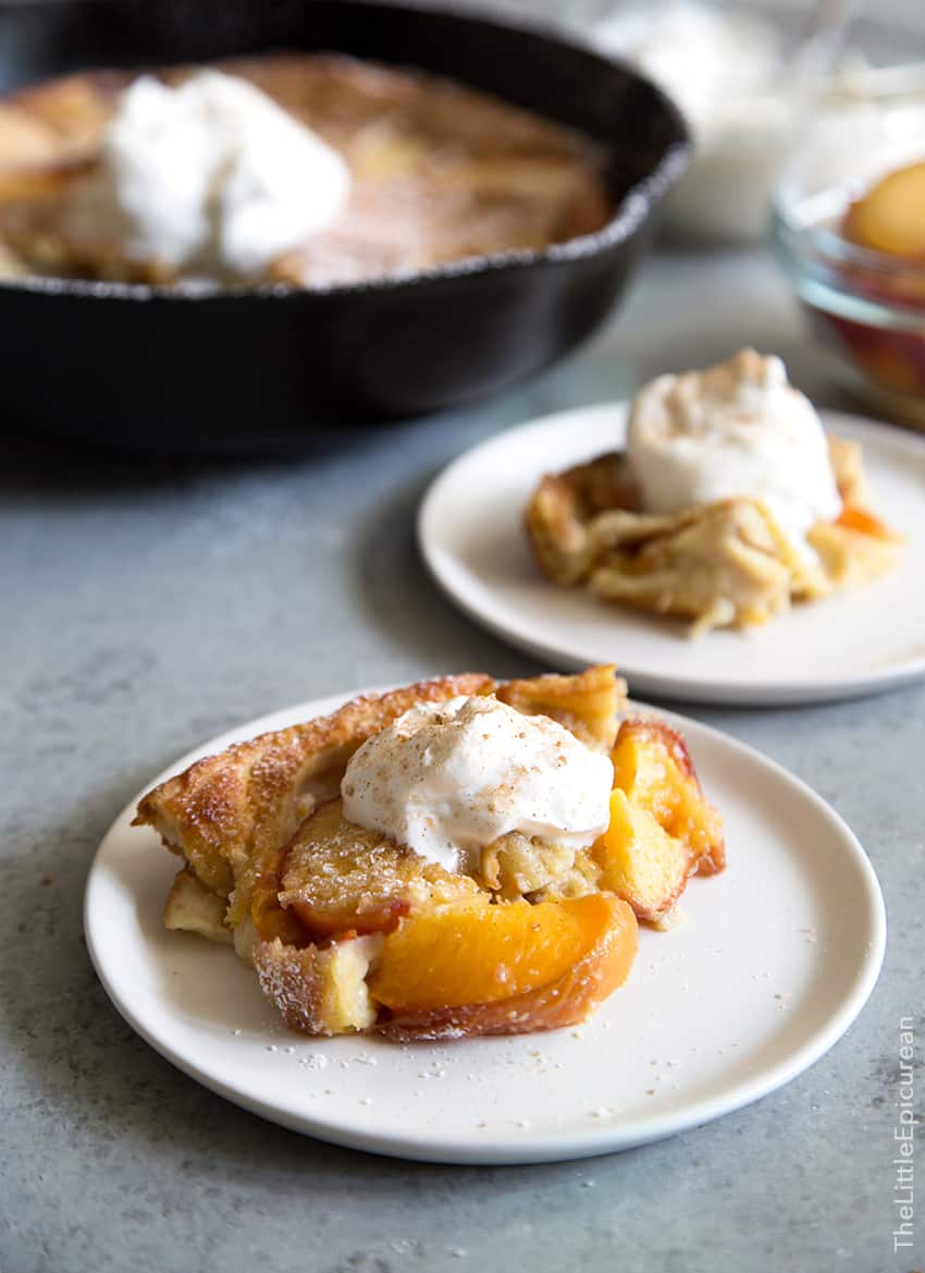 whiskey peach clafoutis garnished with whipped cream on white plate.
