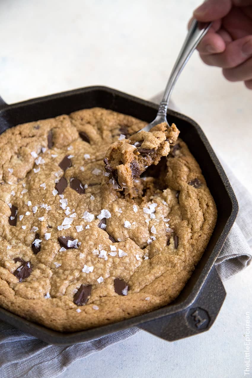 peanut butter chocolate chunk cookie cooked in a skillet being eaten with a spoon.