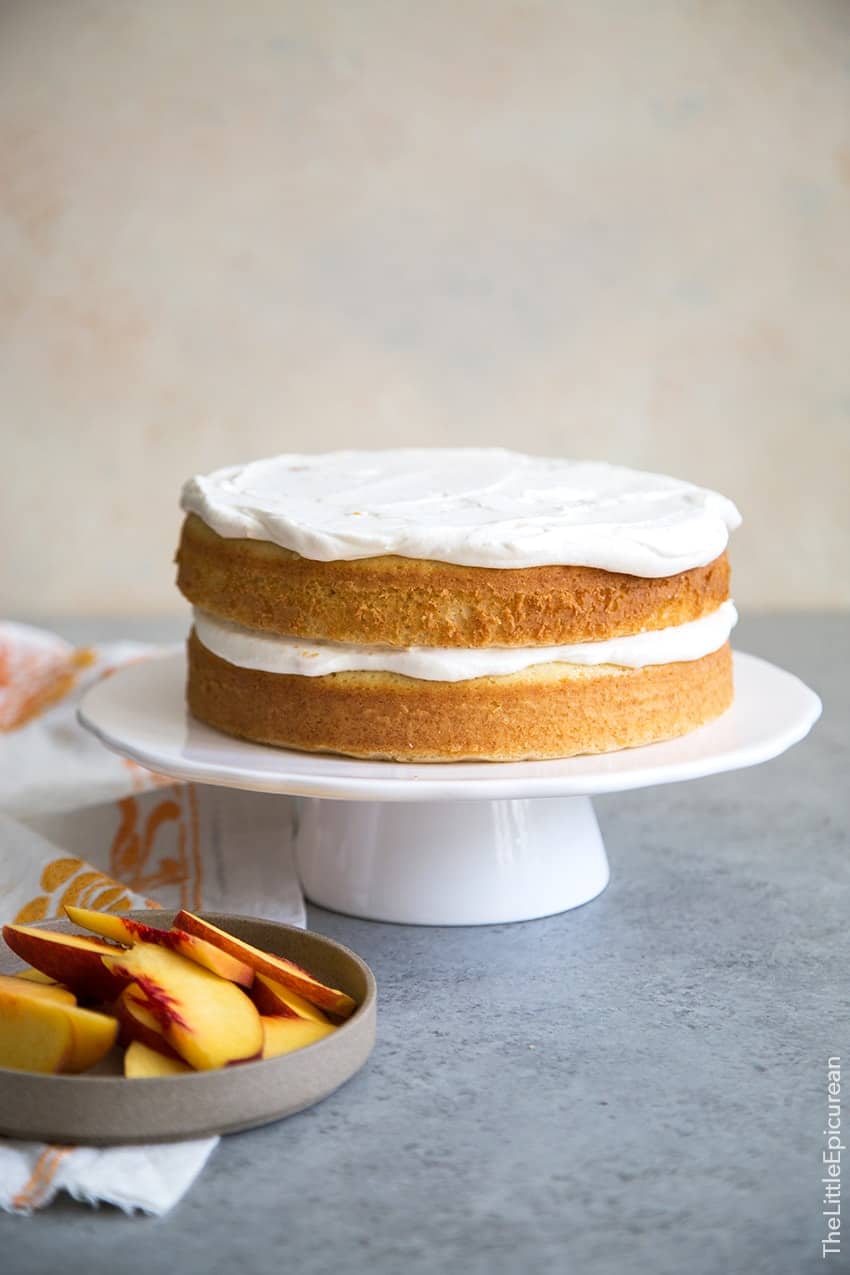 two layer cake frosted with whipped cream on white cake stand. 