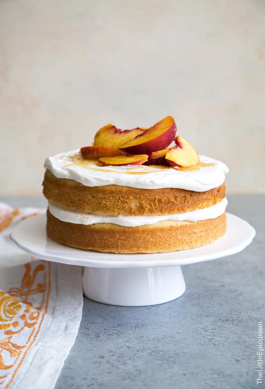 Peach Bellini Cake topped with fresh peach slices on white cake stand.