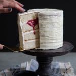 White cake being sliced into with red raspberry blood oozing out.