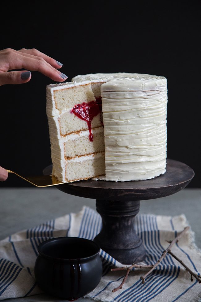 White cake being sliced into with red raspberry blood oozing out.