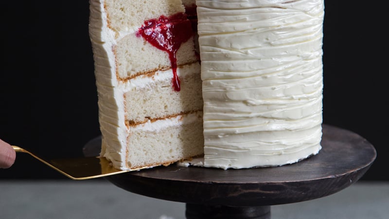 White cake being sliced into with red raspberry blood oozing out.