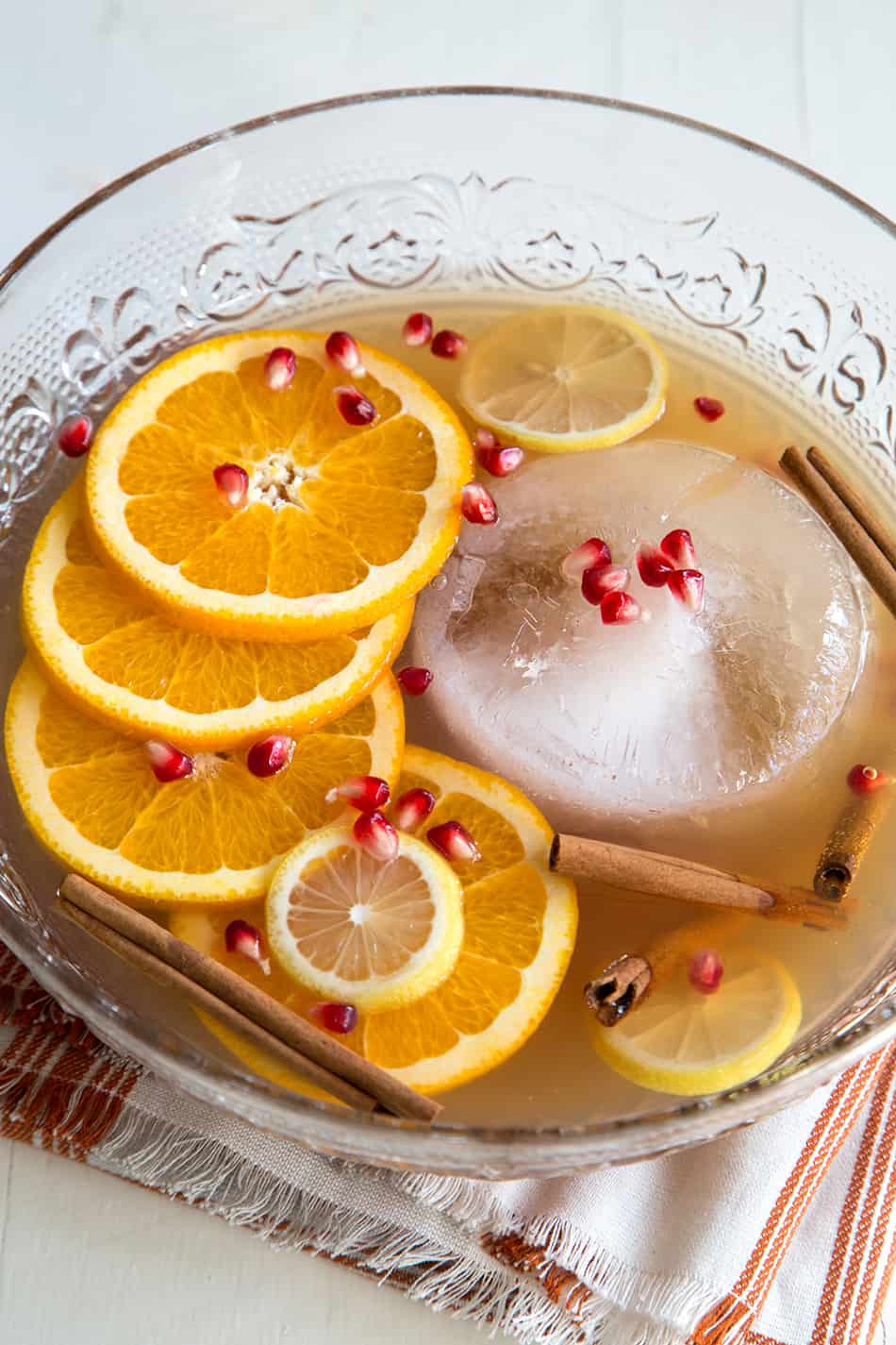 apple ginger punch in glass punch bowl garnished with orange slices and pomegranate seeds. 