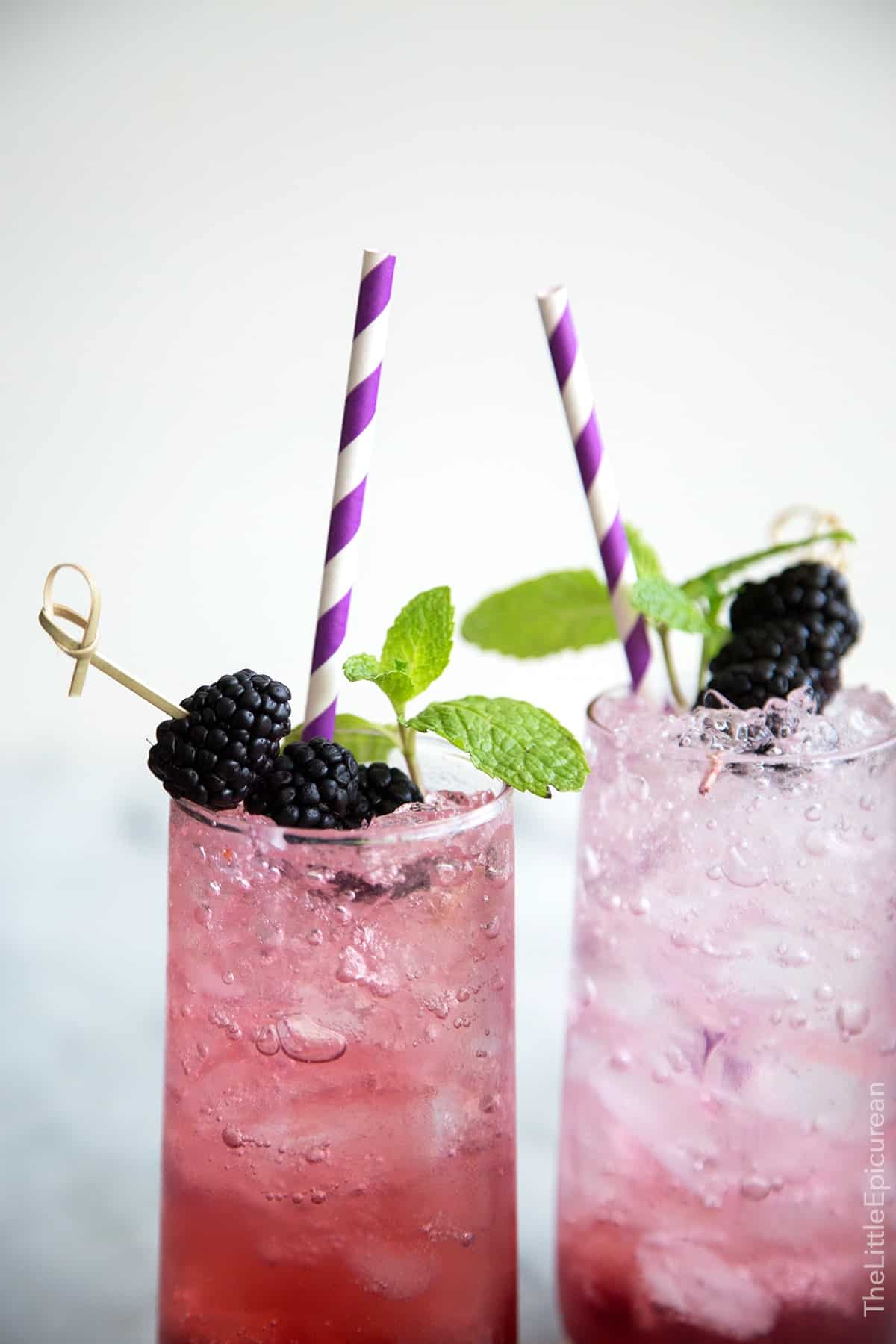 two servings for sparkling blackberry shrub mocktails garnished with fresh blackberries, mint, and purple straw.