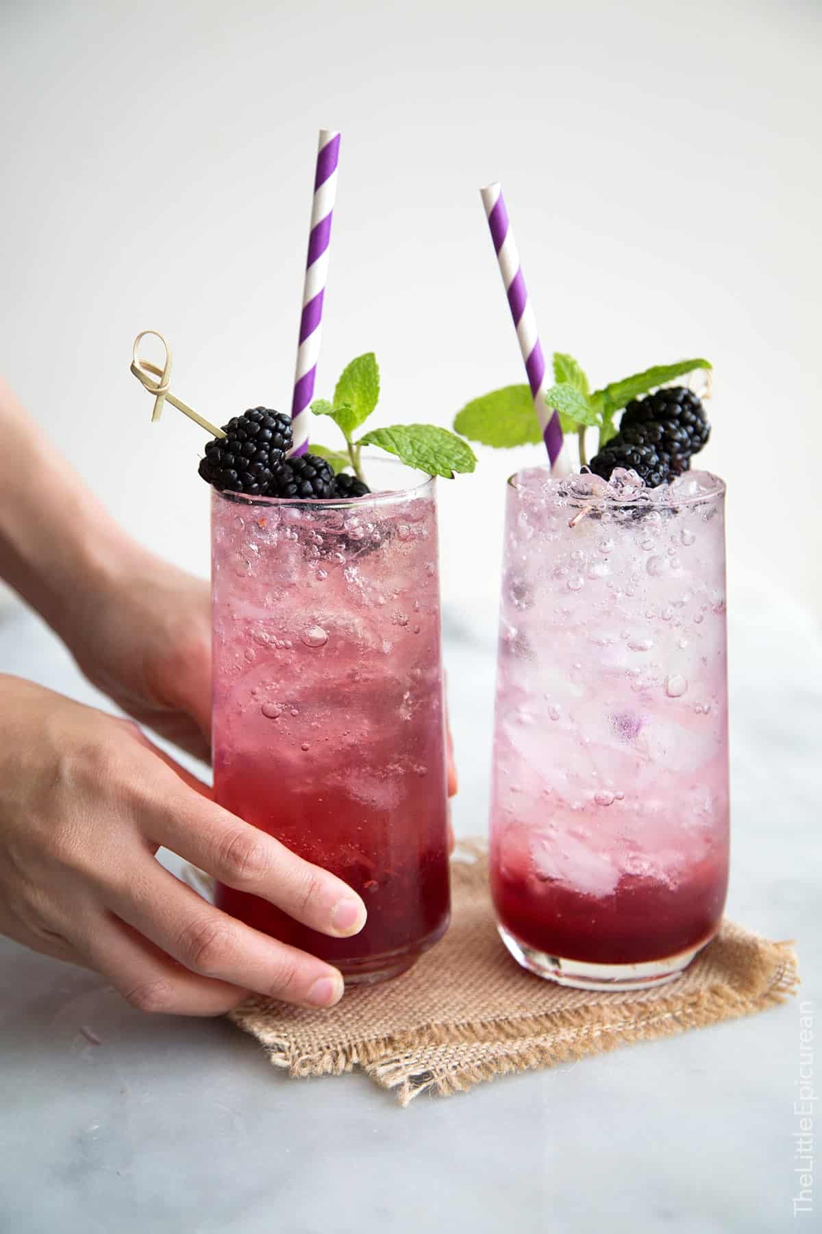 two servings for sparkling blackberry shrub mocktails garnished with fresh blackberries, mint, and purple straw.