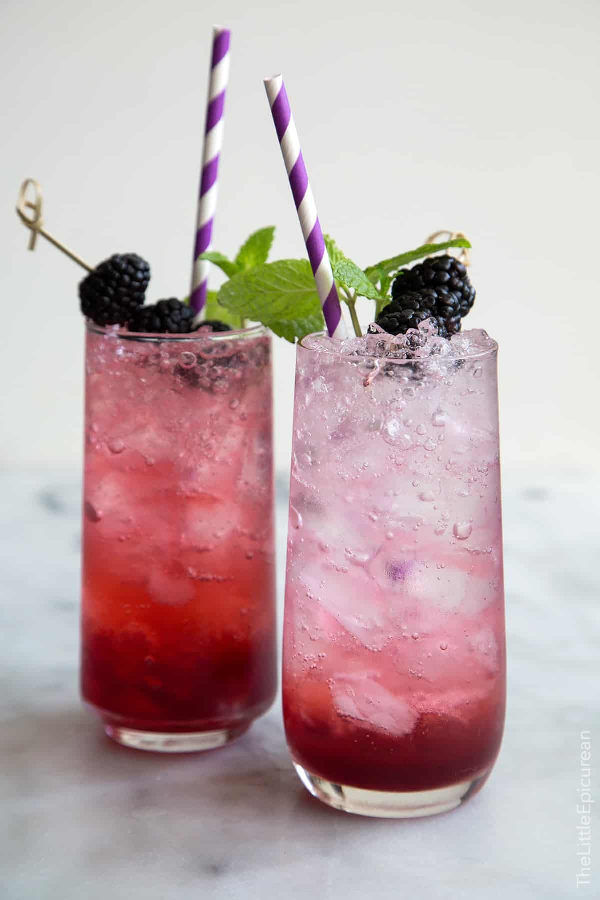 two servings for sparkling blackberry shrub mocktails garnished with fresh blackberries, mint, and purple straw.