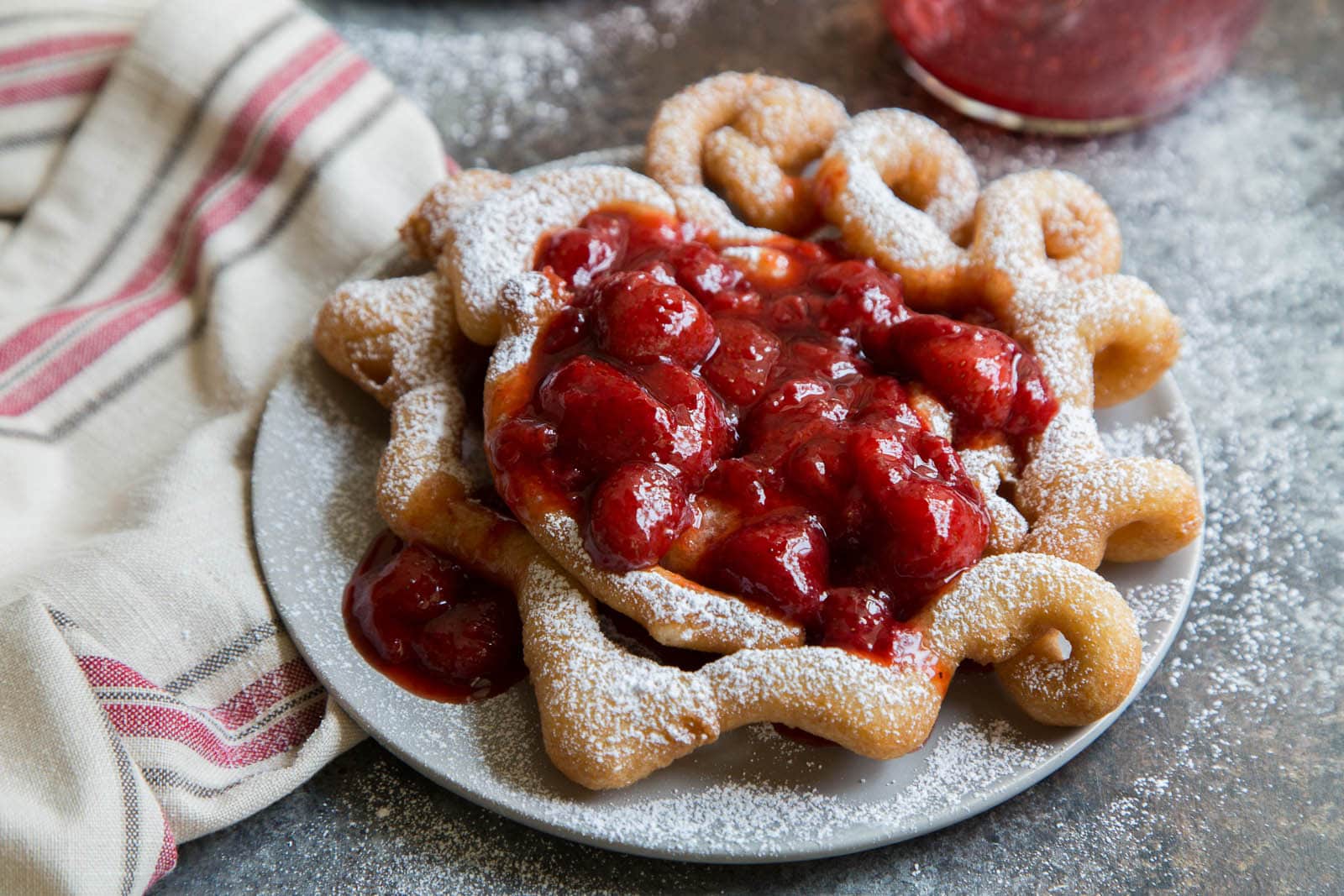 homemade funnel cake topped with strawberry sauce and powdered sugar.