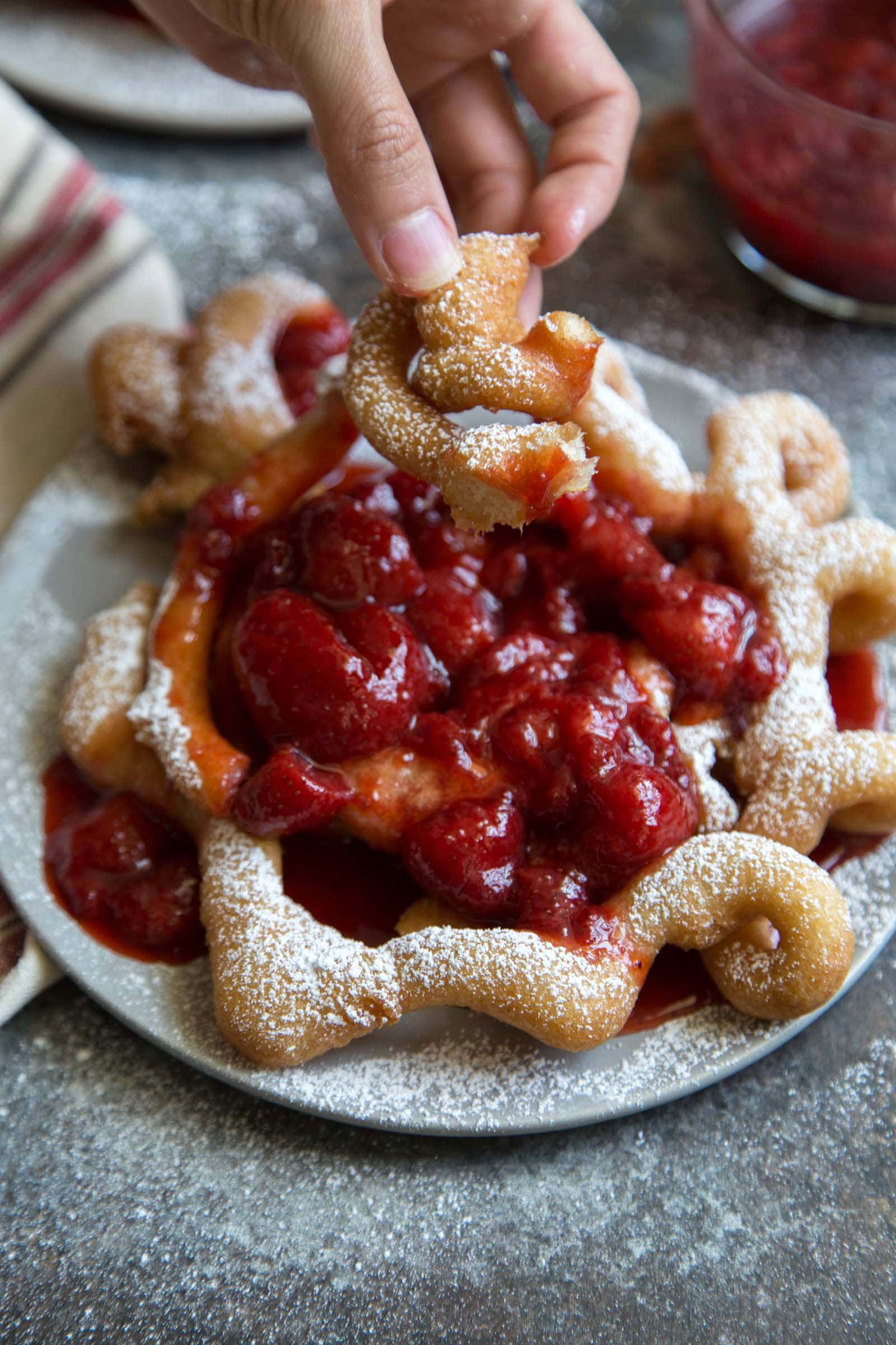 homemade funnel cake topped with strawberry sauce and powdered sugar.