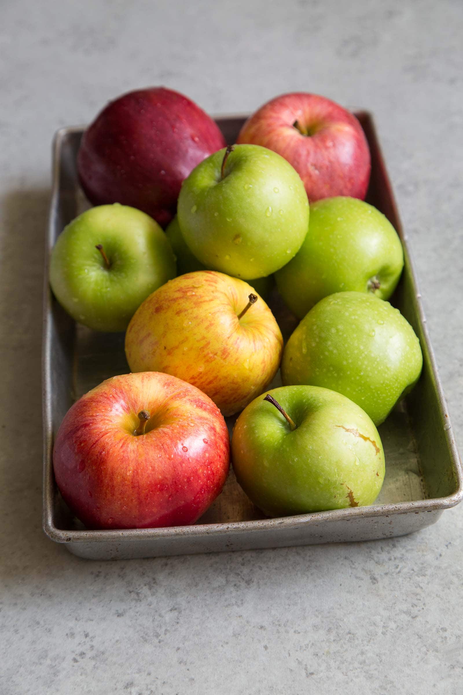 variety of fresh apples in rectangle baking sheet. 
