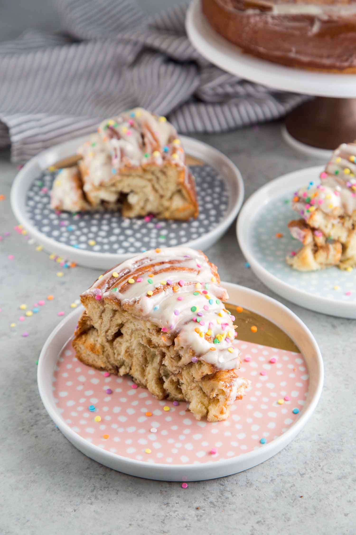 Slice of giant cinnamon roll cake with cream cheese frosting and confetti sprinkles
