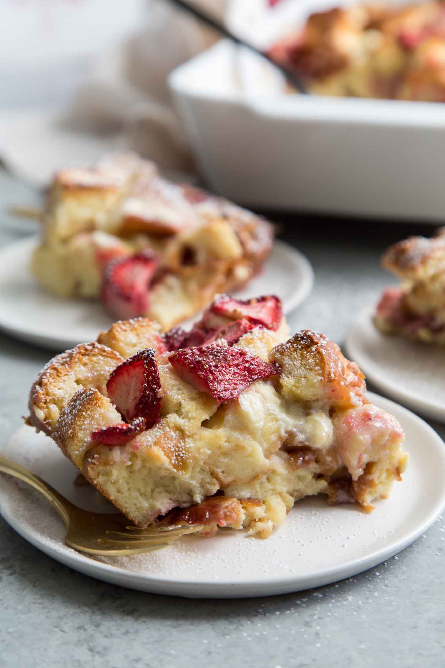 serving of White Chocolate Strawberry Bread Pudding in white dessert plate with gold fork. 