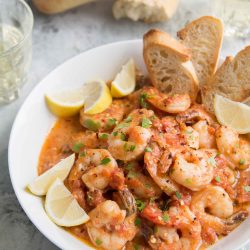 Tomato Shrimp Scampi in a white bowl served with slices of toasted bread.