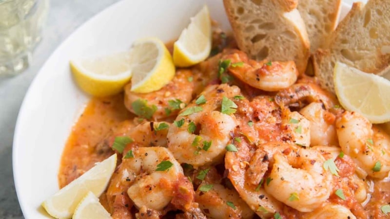 Tomato Shrimp Scampi in a white bowl served with slices of toasted bread.