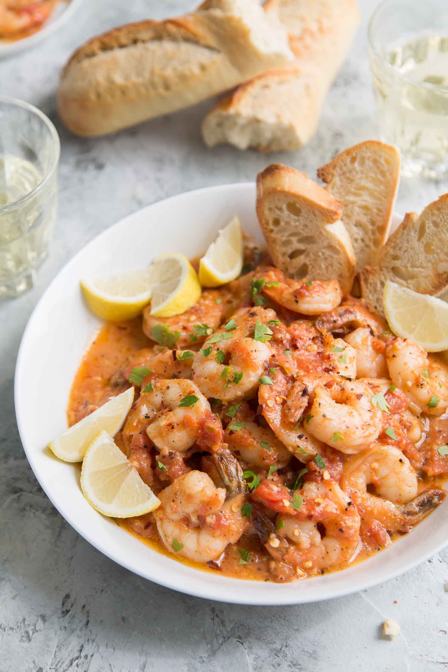 Tomato Shrimp Scampi in a white bowl served with slices of toasted bread.