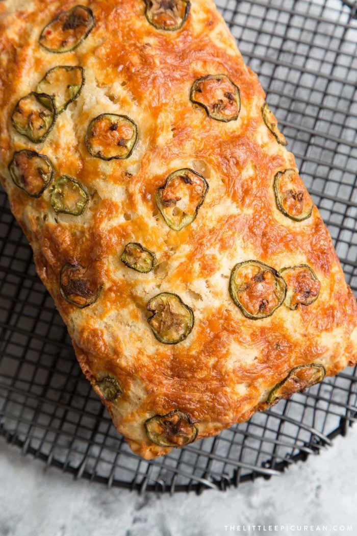 Spicy beer bread loaf topped with sliced jalapeños on black wire rack.