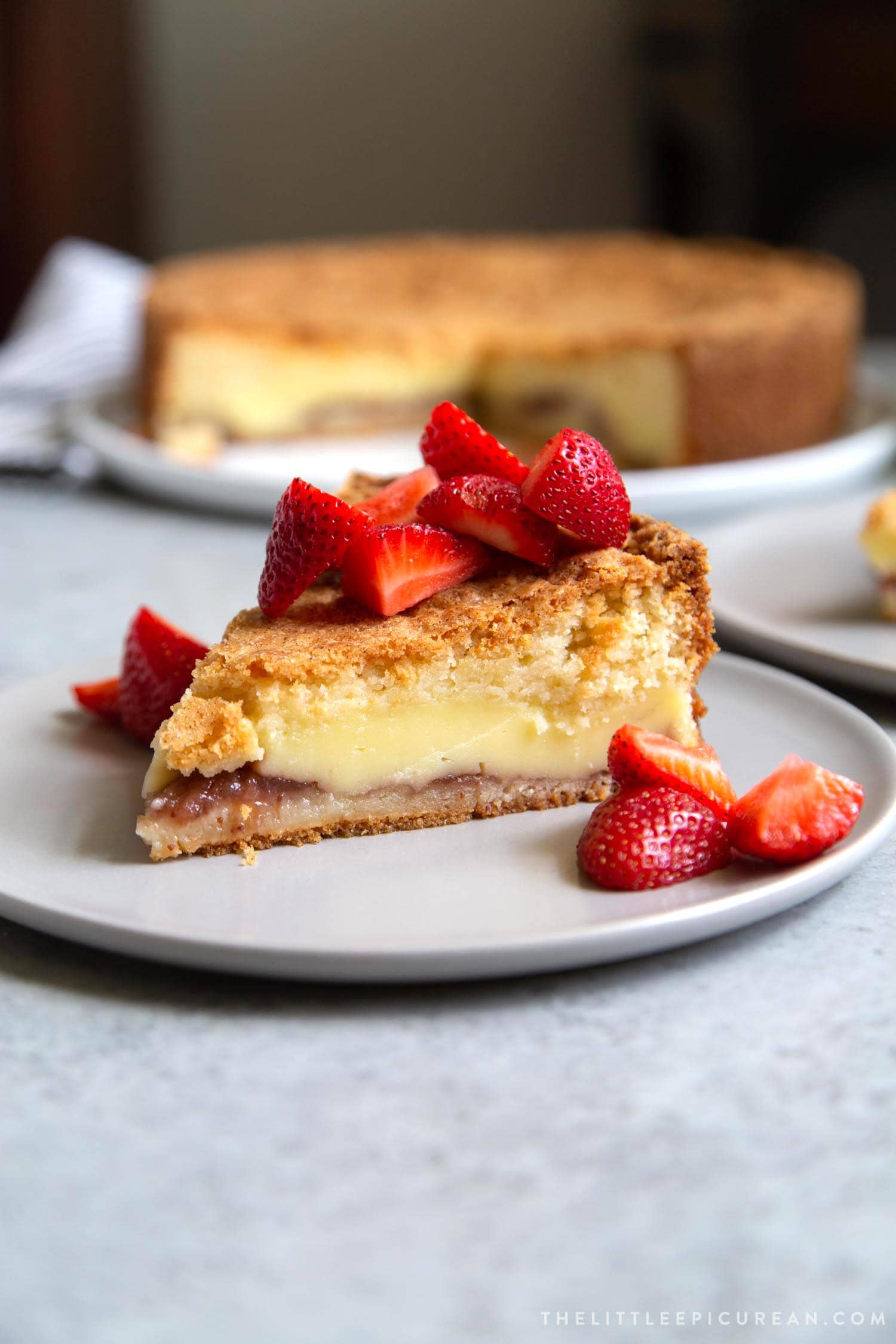 Slice of Basque Cake topped with fresh strawberries. Basque Cake is a buttery cake with strawberry jam and pastry cream filling.