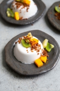 Coconut Panna Cotta served with latik and fresh fruits. Latik is from the Philippines. It is fried coconut milk curds.