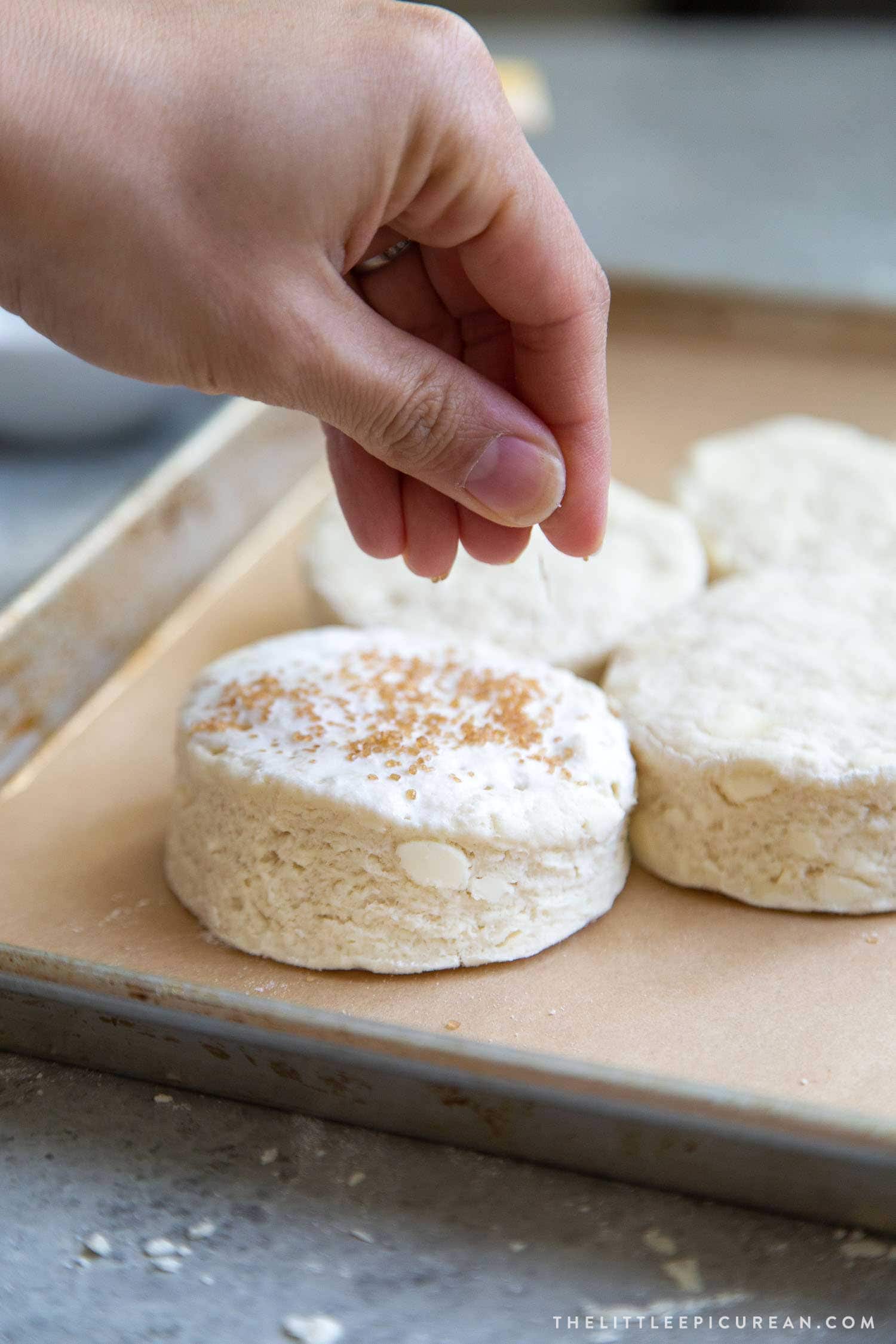 Coconut shortcake biscuits are brushed with cream and topped with turbinado sugar before baking.