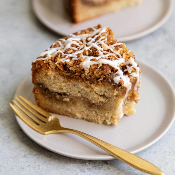 Banana Crumb Cake Slice. Moist banana cake with cinnamon sugar filling topped with walnut oat crumble topping. Finished with maple glaze icing.