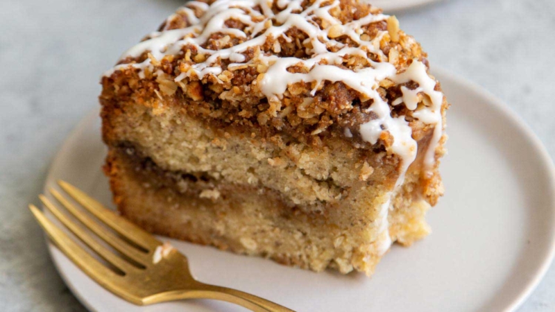 Banana Crumb Cake Slice. Moist banana cake with cinnamon sugar filling topped with walnut oat crumble topping. Finished with maple glaze icing.