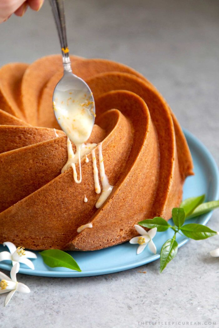 Orange blossom bundt cake drizzled with orange glaze on blue serving plate.