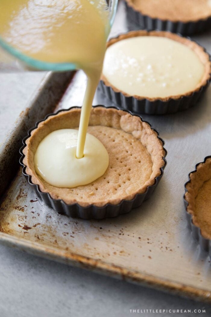custard filling being poured into baked tart shell. 