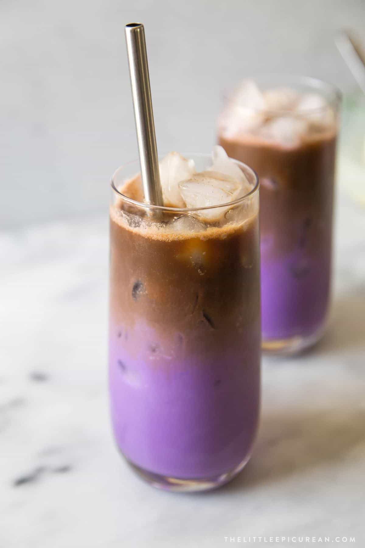 iced ube latte served in glass with metal straw. Shows distinct purple milk bottom and brown espresso topping.