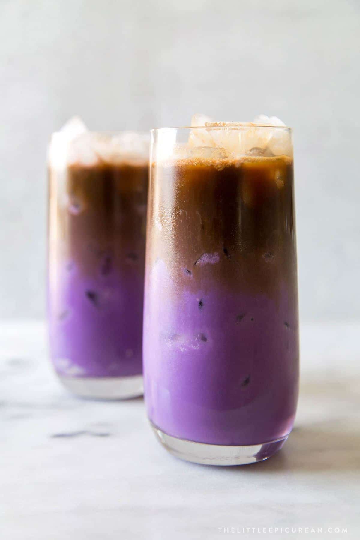 two glasses of iced ube latte. purple milk featured at the bottom with espresso floating on top.