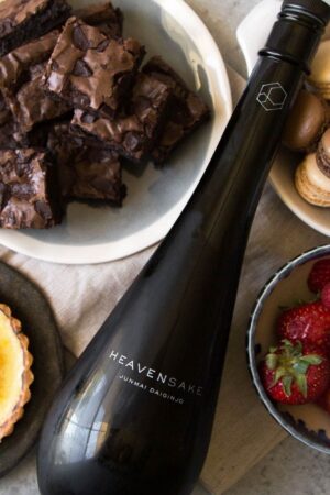 bottle of sake surrounded by creme brulee tart, brownies, macarons, and fresh berries.