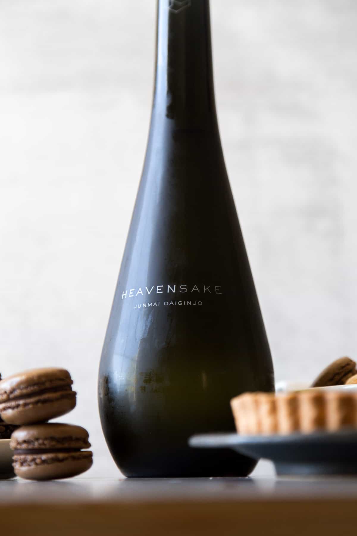 chilled bottle of sake surrounded by chocolate macaron and tart. 