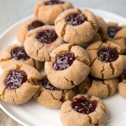 a dozen peanut butter thumbprints on a white plate.