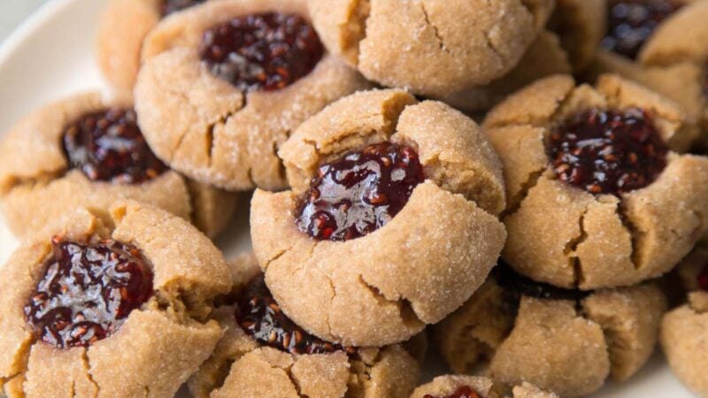 a dozen peanut butter thumbprints on a white plate.