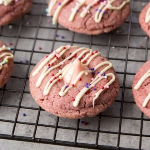 strawberry kiss cookies with white chocolate drizzle and assorted colorful sprinkles.