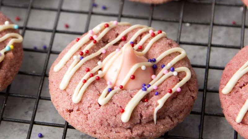 strawberry kiss cookies with white chocolate drizzle and assorted colorful sprinkles.