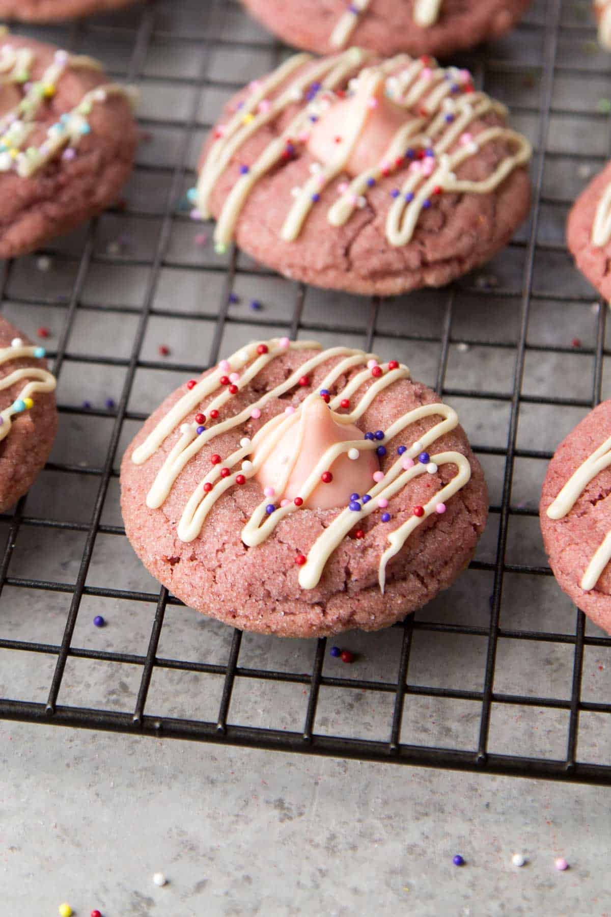 strawberry kiss cookies with white chocolate drizzle and assorted colorful sprinkles.