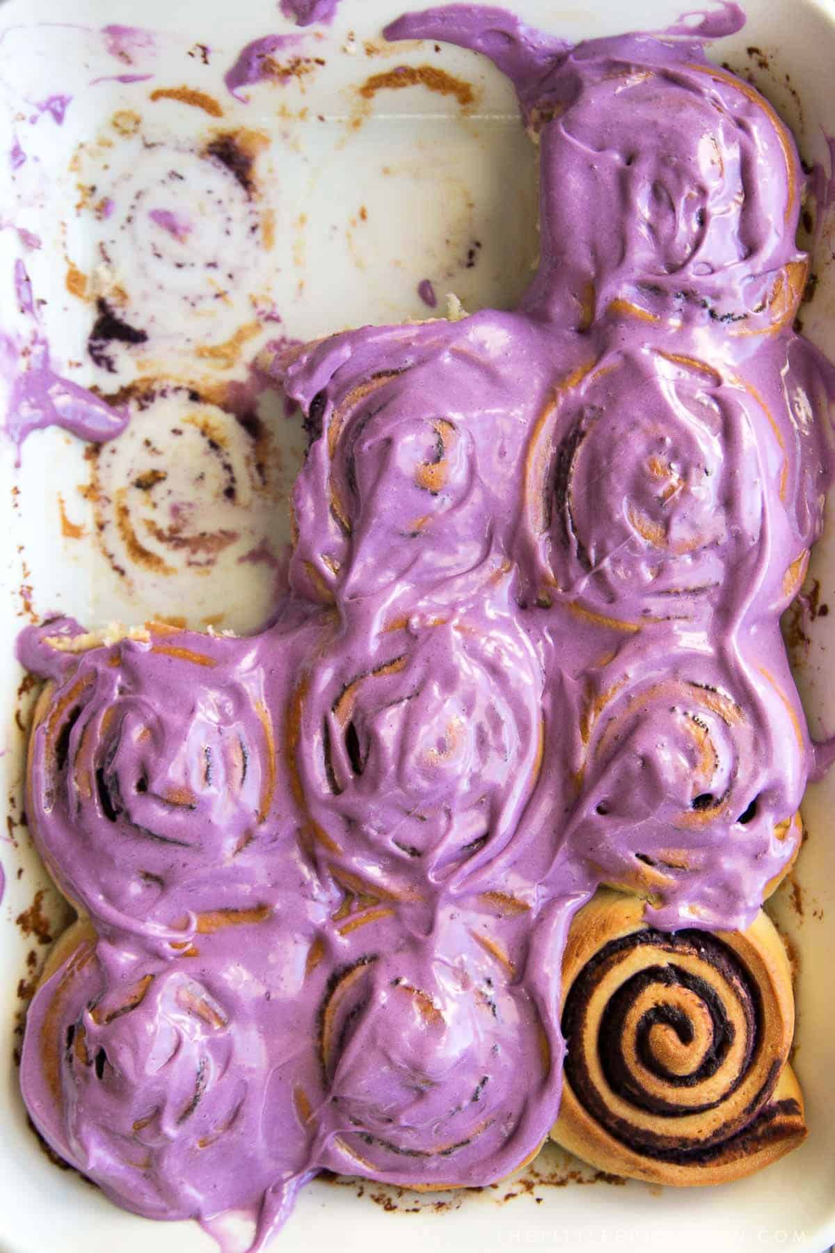 ube bread rolls in white baking pan topped with ube cream cheese frosting.