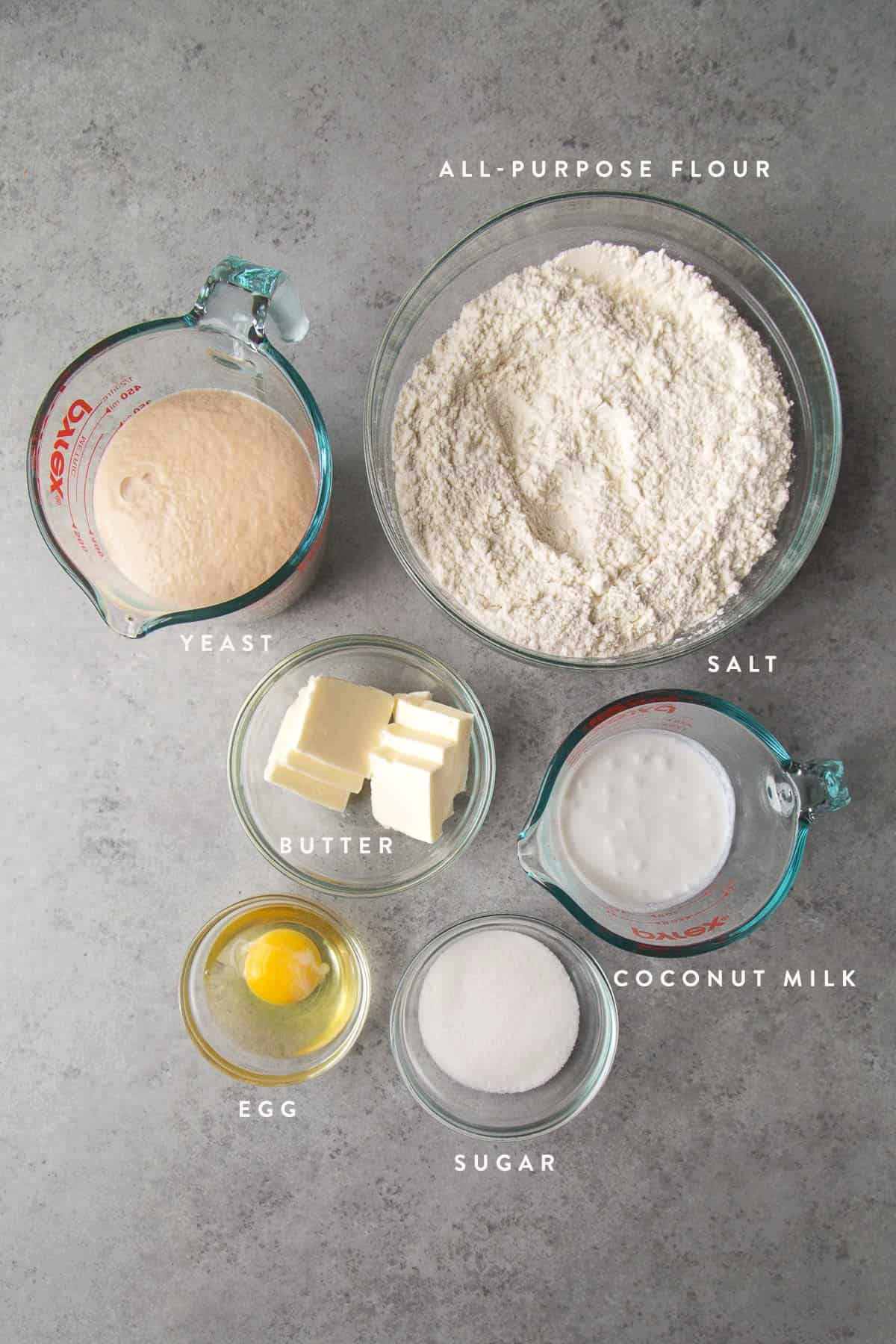 overhead of bread dough ingredients including flour, yeast, and coconut milk.