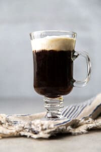 Irish coffee topped with lightly sweetened whipped cream in clear mug.