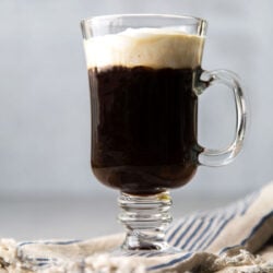 Irish coffee topped with lightly sweetened whipped cream in clear mug.