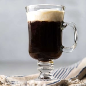 Irish coffee topped with lightly sweetened whipped cream in clear mug.