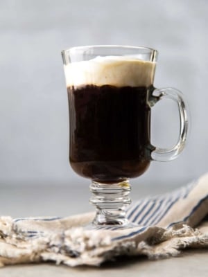 Irish coffee topped with lightly sweetened whipped cream in clear mug.