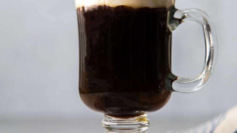 Irish coffee topped with lightly sweetened whipped cream in clear mug.