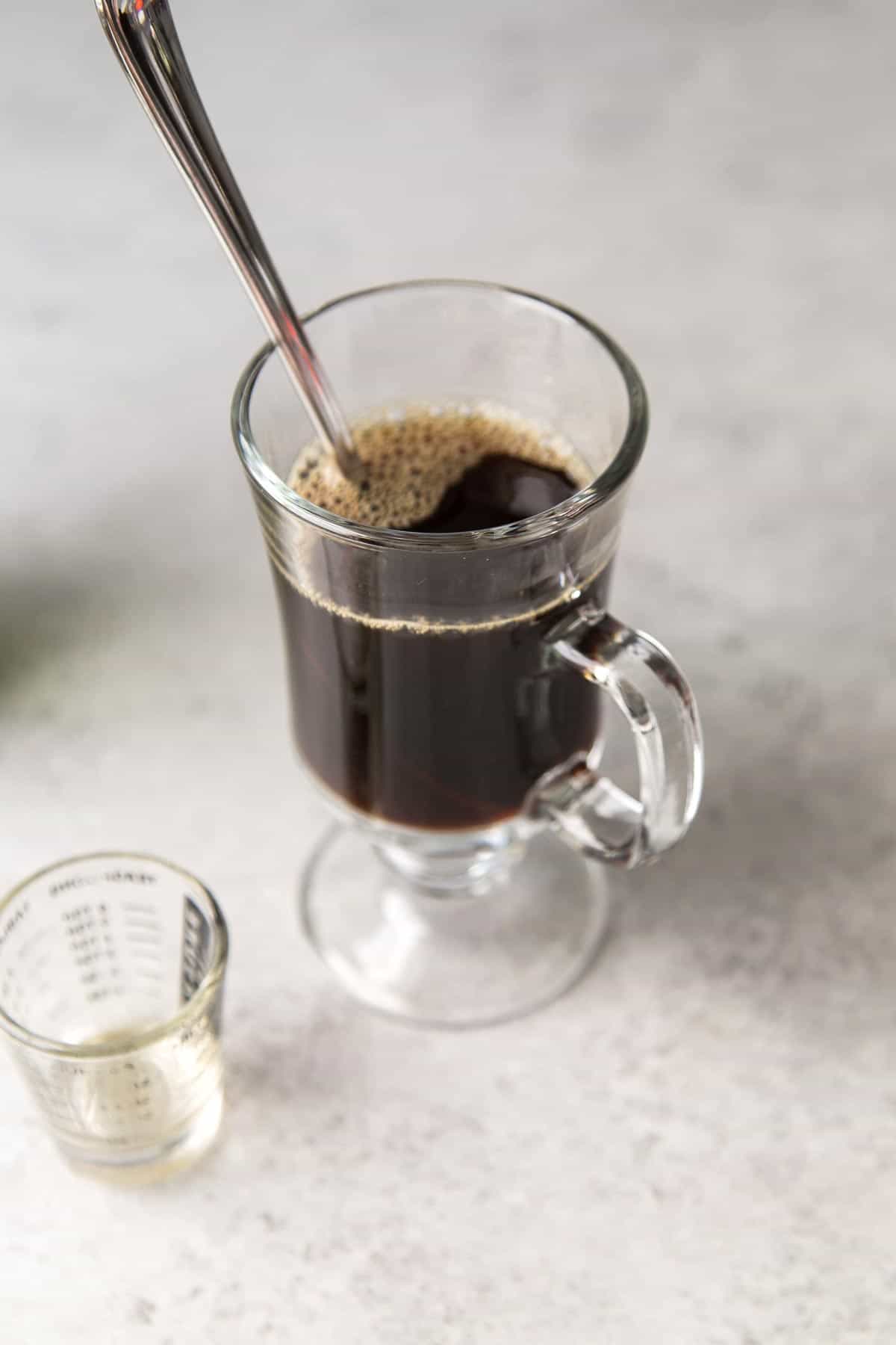 clear mug filled with hot coffee and stirring spoon.